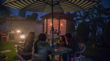 An outdoor patio with a gazebo, chairs, and tables under striped umbrellas.