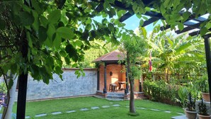 A garden with a brick wall, a pergola, and a small patio area with a table and chairs. - Hotel Ananda Inn (Lumbini)