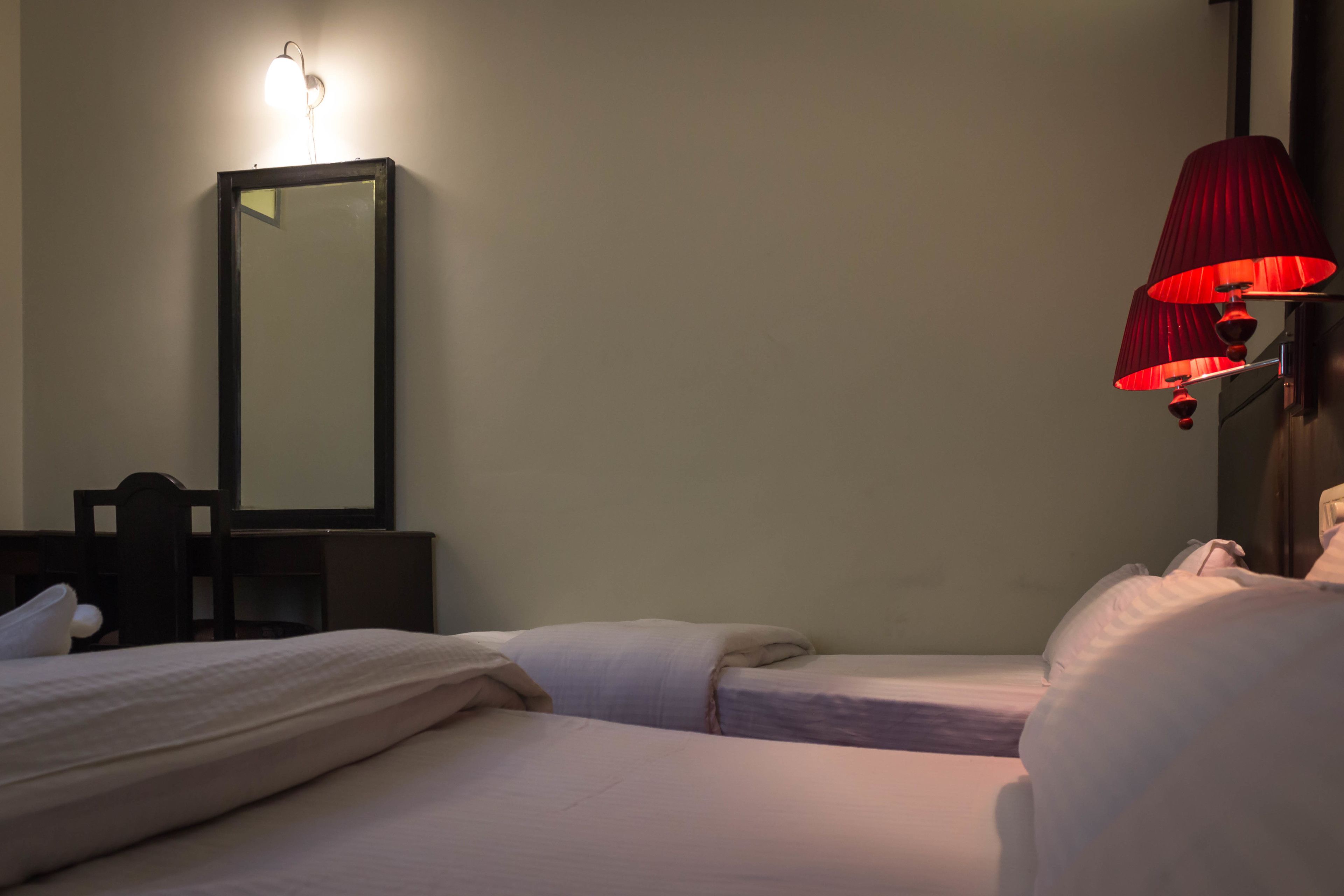 A hotel room with two beds, a mirror, a desk, and a red lamp.