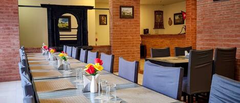 A long dining table with chairs, a brick wall, and a ceiling fan.