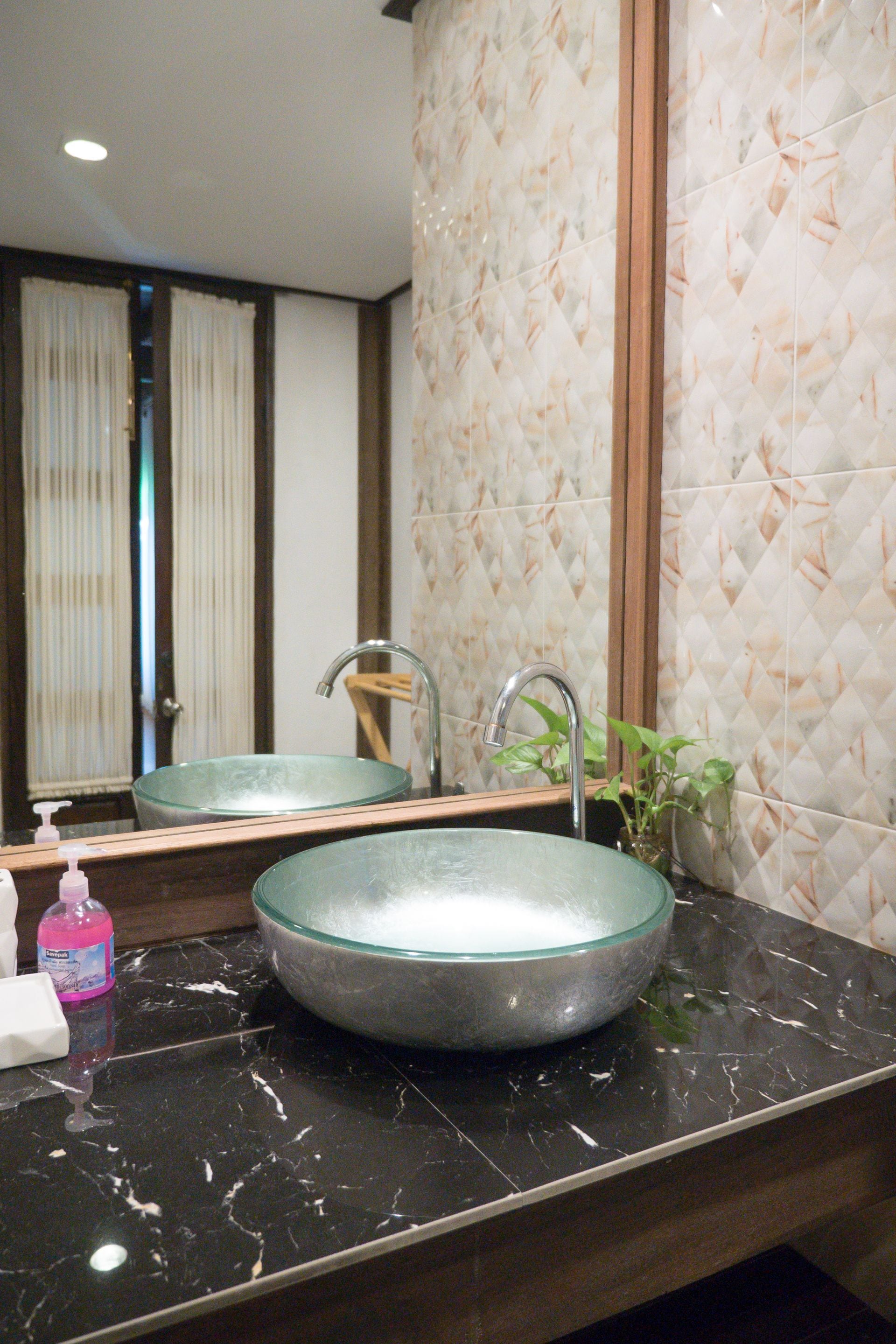 A bathroom with a glass bowl sink, a mirror, a faucet, a soap dispenser, and a potted plant.