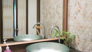 A bathroom with a glass bowl sink, a mirror, a faucet, a soap dispenser, and a potted plant.