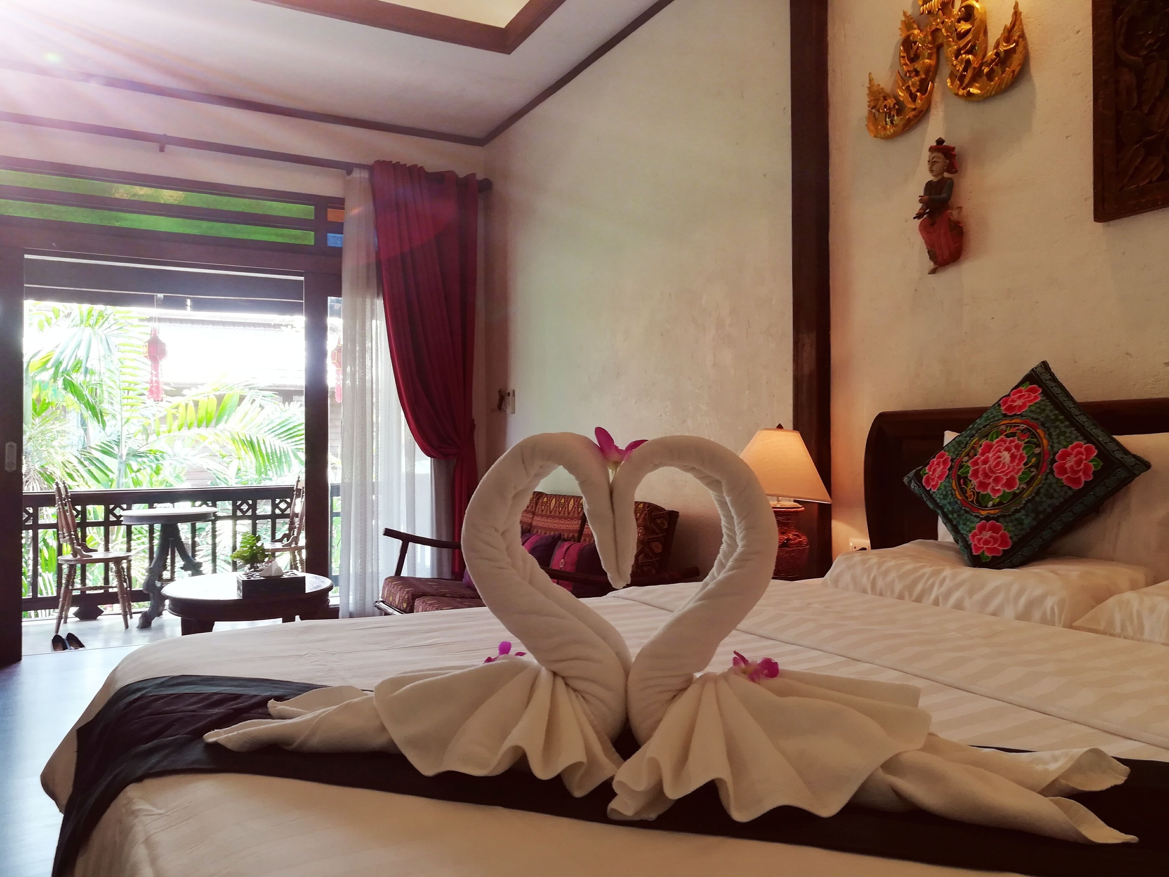 A hotel room with a bed, a sitting area with chairs and a table, and a view of greenery outside.