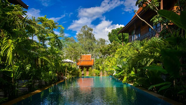Ein Pool, umgeben von üppiger Vegetation und einem Gebäude mit rotem Dach.