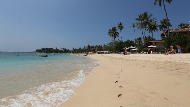 A beach with clear turquoise water, palm trees, and beach umbrellas. - The Villa Hotel (Unawatuna)