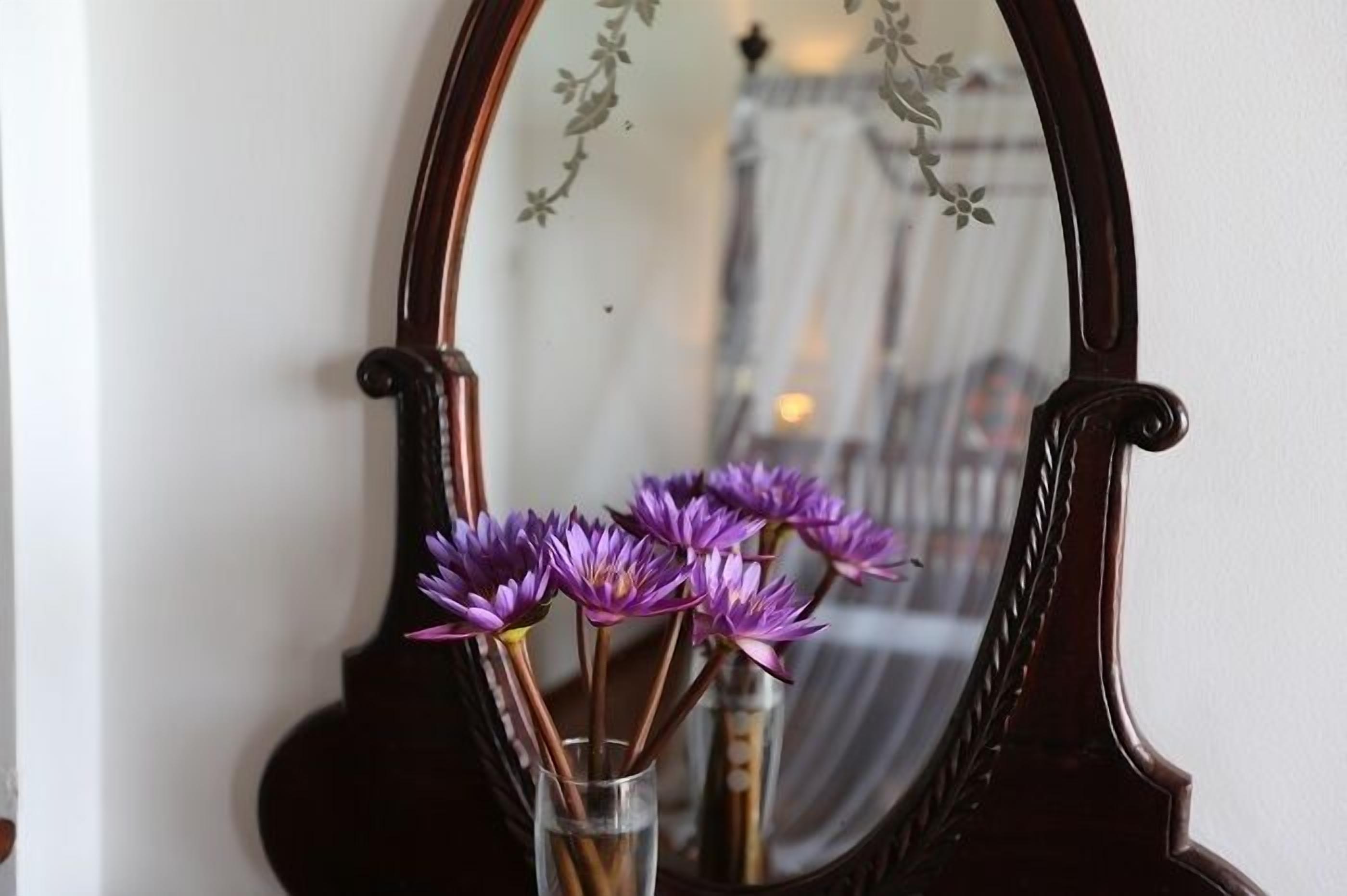 A mirror with a floral design, reflecting a room with a bed and a window.