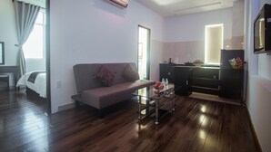 A modern living room with a sofa, a glass coffee table, and a kitchen area with a refrigerator and cabinets. - Rio Hotel (Da Nang)