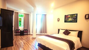 A hotel room with a wooden floor, a bed with white bedding and a dark headboard, two chairs, a small table, and a window with curtains. - Rio Hotel (Da Nang)