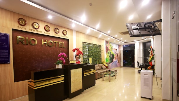 A hotel reception area with a wooden reception desk, a sofa, and a coffee table. - Rio Hotel (Da Nang)