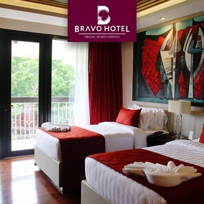 A hotel room with two beds, a balcony, and a painting on the wall. - Bravo Hotel and Resorts (Sibulan)