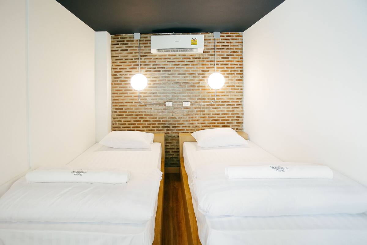 A room with two single beds, a brick wall, and an air conditioning unit.