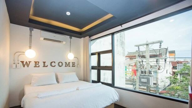 A modern hotel room with a large bed, a "WELCOME" sign, and a view of the cityscape through large windows. - Give Me 5 Hostel (Chiang Mai)