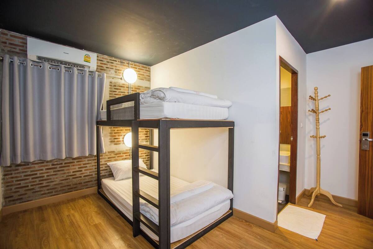 A bunk bed room with a brick wall, a ceiling fan, and a coat rack.