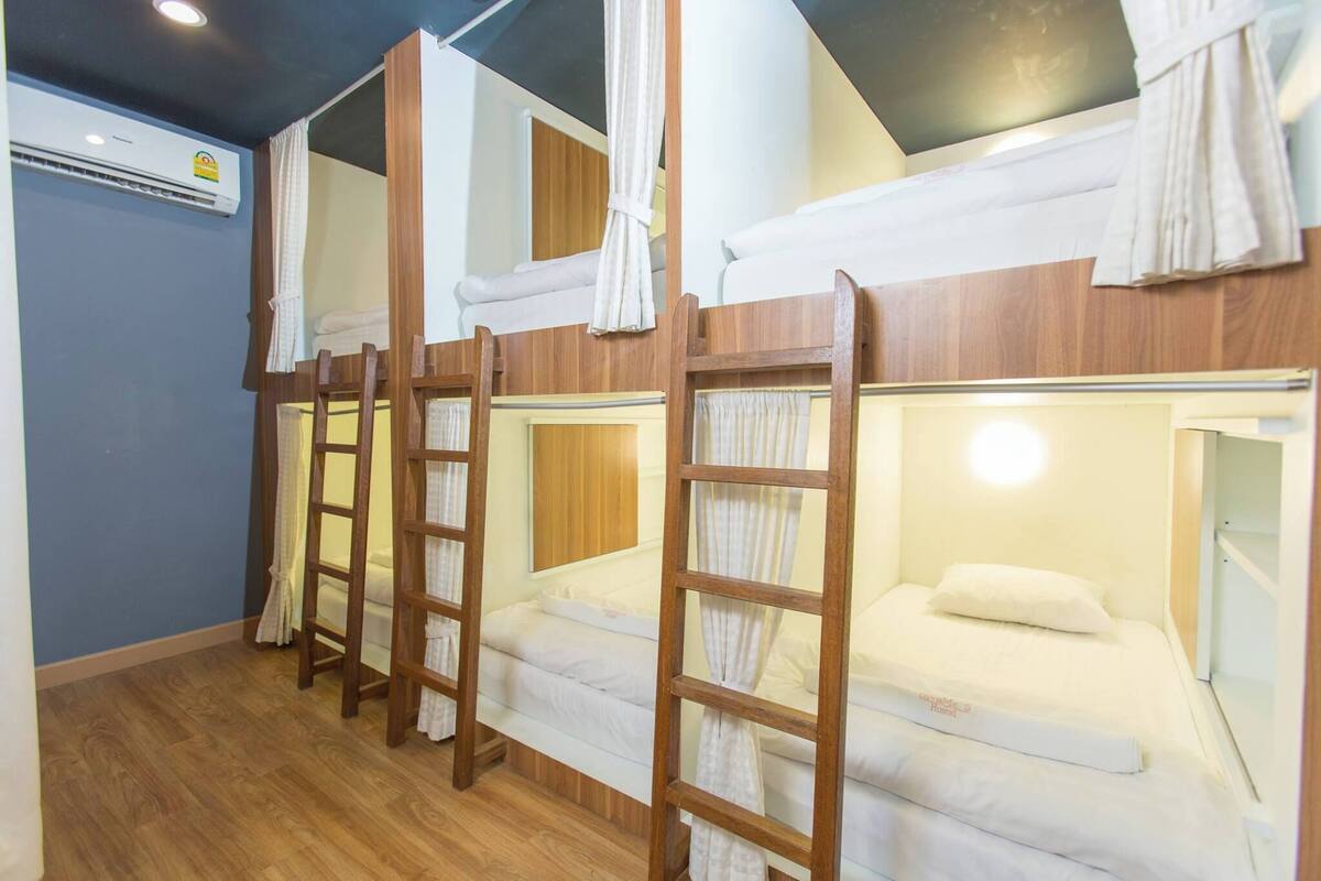 A dormitory room with bunk beds, wooden ladders, and white curtains.