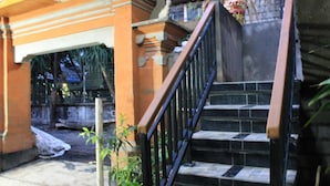 A staircase with black railings leading to an upper level, surrounded by orange walls and potted plants. - Chillin Kuta Homestay (Tuban)