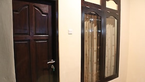 A dark wooden door with a silver handle and a keyhole, adjacent to a window with a patterned curtain. - Chillin Kuta Homestay (Tuban)