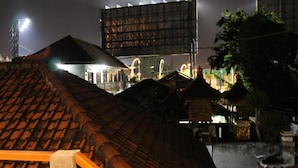A night view of a building with a tiled roof, a large billboard, and a well-lit area in the background. - Chillin Kuta Homestay (Tuban)