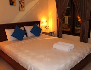 A neatly made bed with white and blue pillows, a rolled white towel, and a nightstand with a lamp and two bottles. - Chillin Kuta Homestay (Tuban)