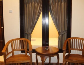 A room with a bed, two wooden chairs, and a small round table.