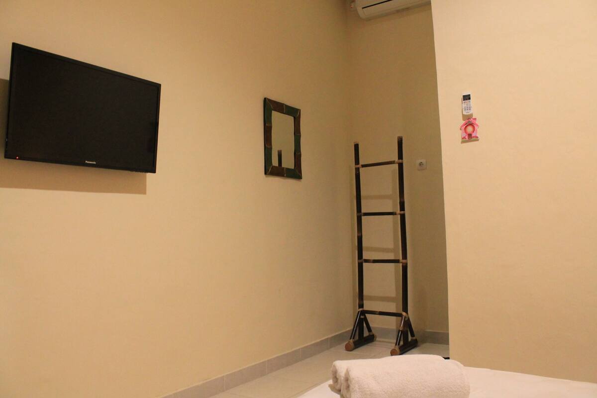Une chambre d’hôtel équipée d’un téléviseur à écran plat fix é au mur, d’un petit miroir et d’une échelle appuyée contre le mur.