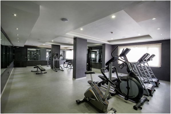 Uma academia com equipamentos de ginástica, um espelho grande e uma janela com luz natural.