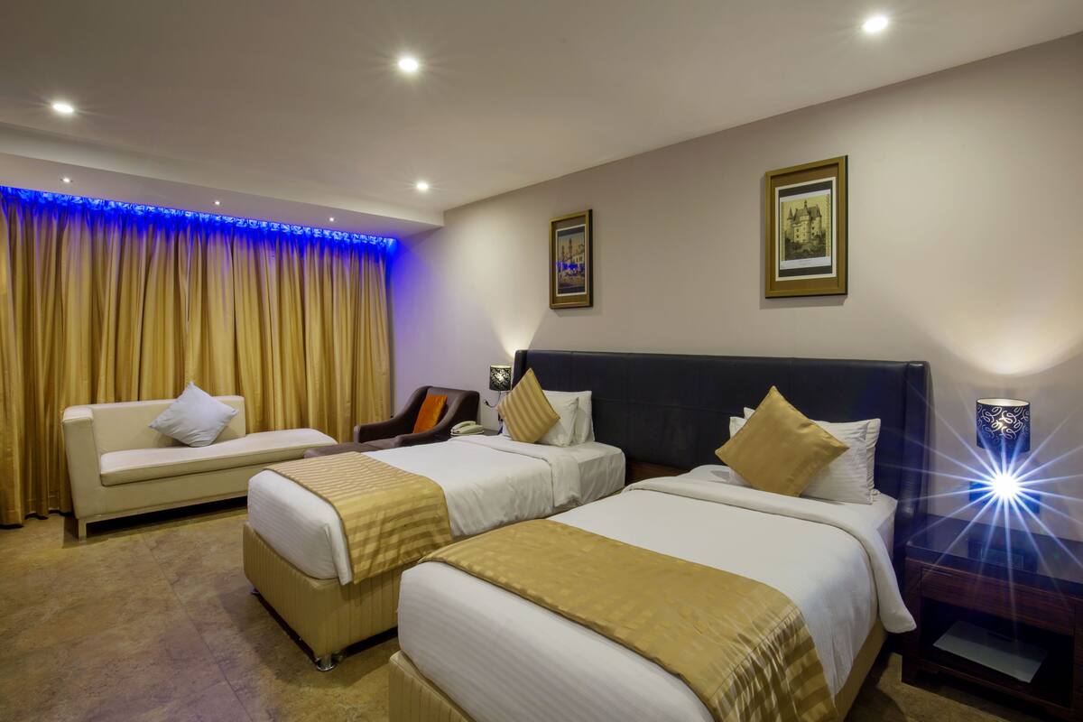 Ein Hotelzimmer mit zwei Betten, einem Schlafsofa, einem Sessel und einem Schreibtisch.