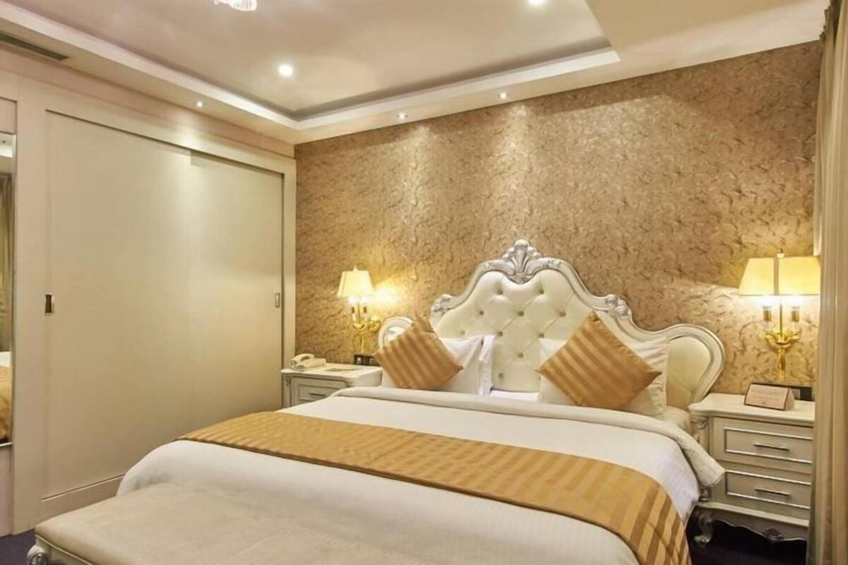 Ein Hotelzimmer mit einem großen Bett, einem Spiegel, einem Nachttisch mit Lampe und einer strukturierten Wand.