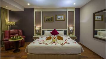 Habitación de hotel con una cama grande, un sillón de cuero rojo, una mesita con un arreglo floral y dos lámparas de noche.