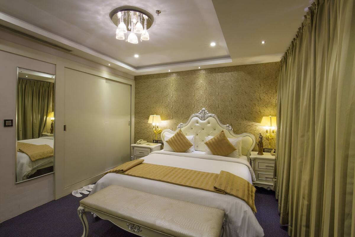 Ein Hotelzimmer mit einem großen Bett, einem Nachttisch mit Lampe, einem Spiegel und einer Chandelüster.