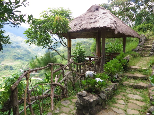 A rustic thatched-roof structure surrounded by lush greenery and stone steps. - Native Village Inn (Banaue)
