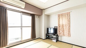 A room with tatami flooring, a sliding glass door, a flat-screen TV on a stand, and a wall-mounted air conditioner. - Hotel SSK Osaka Naniwa (Osaka)