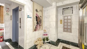 A hotel lobby with marble flooring, a blue elevator, a decorative wall hanging, a small shelf with plants, and a fire extinguisher. - Hotel SSK Osaka Naniwa (Osaka)