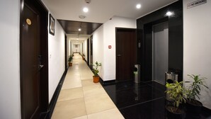 Un pasillo largo y estrecho en un hotel, con suelo de baldosas, plantas en macetas y puertas a ambos lados.