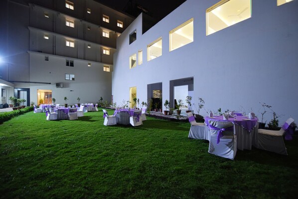 A courtyard with tables and chairs set up for an event, surrounded by a building with multiple windows and a door.