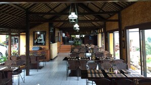 A restaurant with a thatched roof, wooden tables and chairs, and a view of the outdoors. - Pacung Indah Hotel and Restaurant (Baturiti)