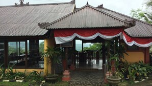A building with a corrugated metal roof, a covered entrance with red and white drapes, and a sign indicating a strawberry dessert. - Pacung Indah Hotel and Restaurant (Baturiti)