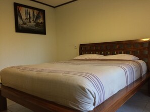 Un lit simple avec une tête de lit en bois, dans une pièce aux murs unis, avec un tableau encadré accroché au-dessus.