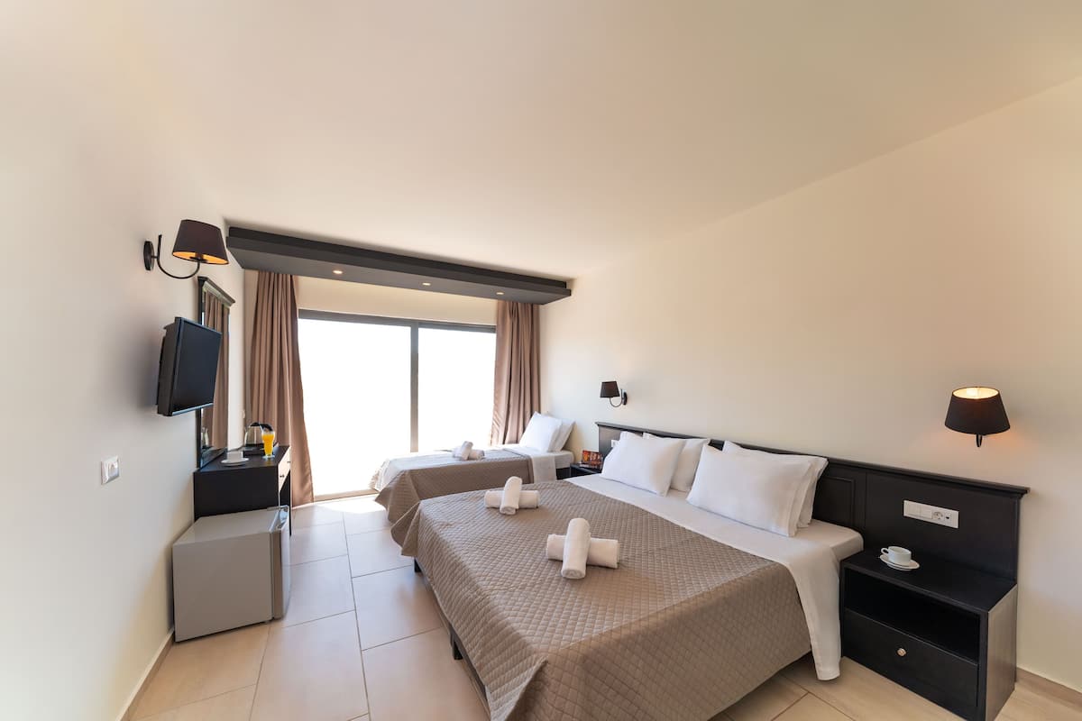 Une chambre d’hôtel avec deux lits, une télévision, un petit bureau et une fenêtre avec des rideaux.