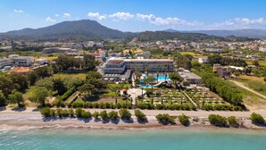 Vista aérea de un hotel frente al mar, con piscina, jardines ajardinados y una playa.