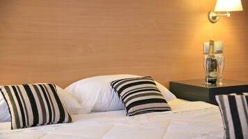 A neatly made bed with striped pillows, a bedside table with a bottle and glasses, and a wall-mounted lamp.