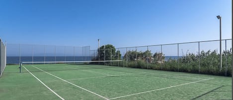 A tennis court with a clear view of the ocean and a fence enclosing the area.
