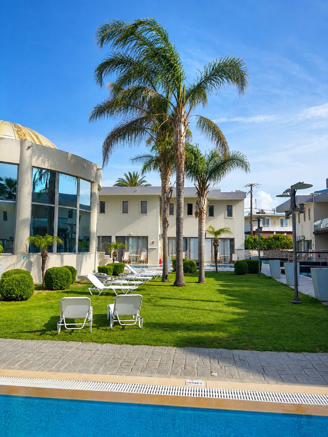 A hotel with a swimming pool, palm trees, and lounge chairs.