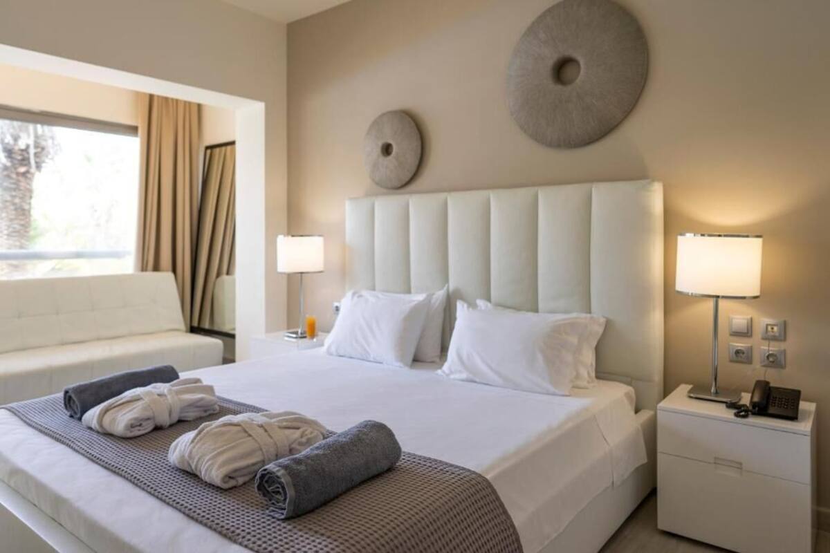 Ein Hotelzimmer mit einem großen Bett, zwei Nachttischlampen, einem Nachttisch mit Telefon und einem Fenster mit Vorhängen.