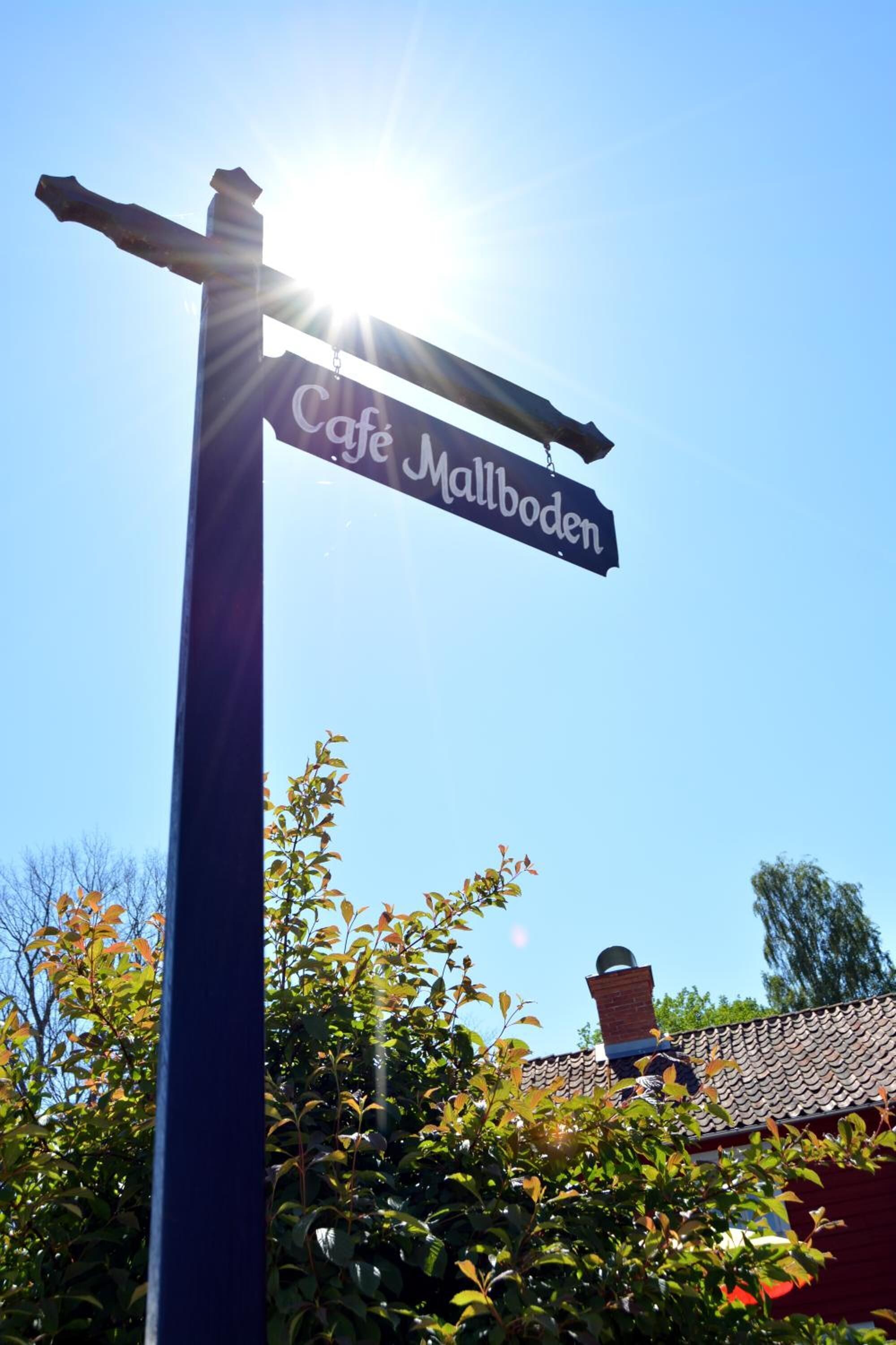Señal de Café Mallboden con un cielo azul despejado y luz solar al fondo.
