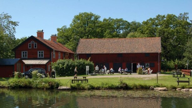 Een rood gebouw met een pannendak, een klein vijvertje ervoor en een picknickplaats met banken.