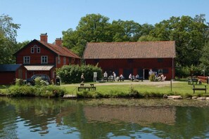 A red building with a tiled roof, a small pond in front, and a picnic area with benches. - Mallboden Café & Vandrarhem (Motala)