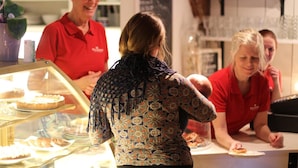 Iemand in een geruit shirt staat bij een toonbank met een vitrine vol gebak.