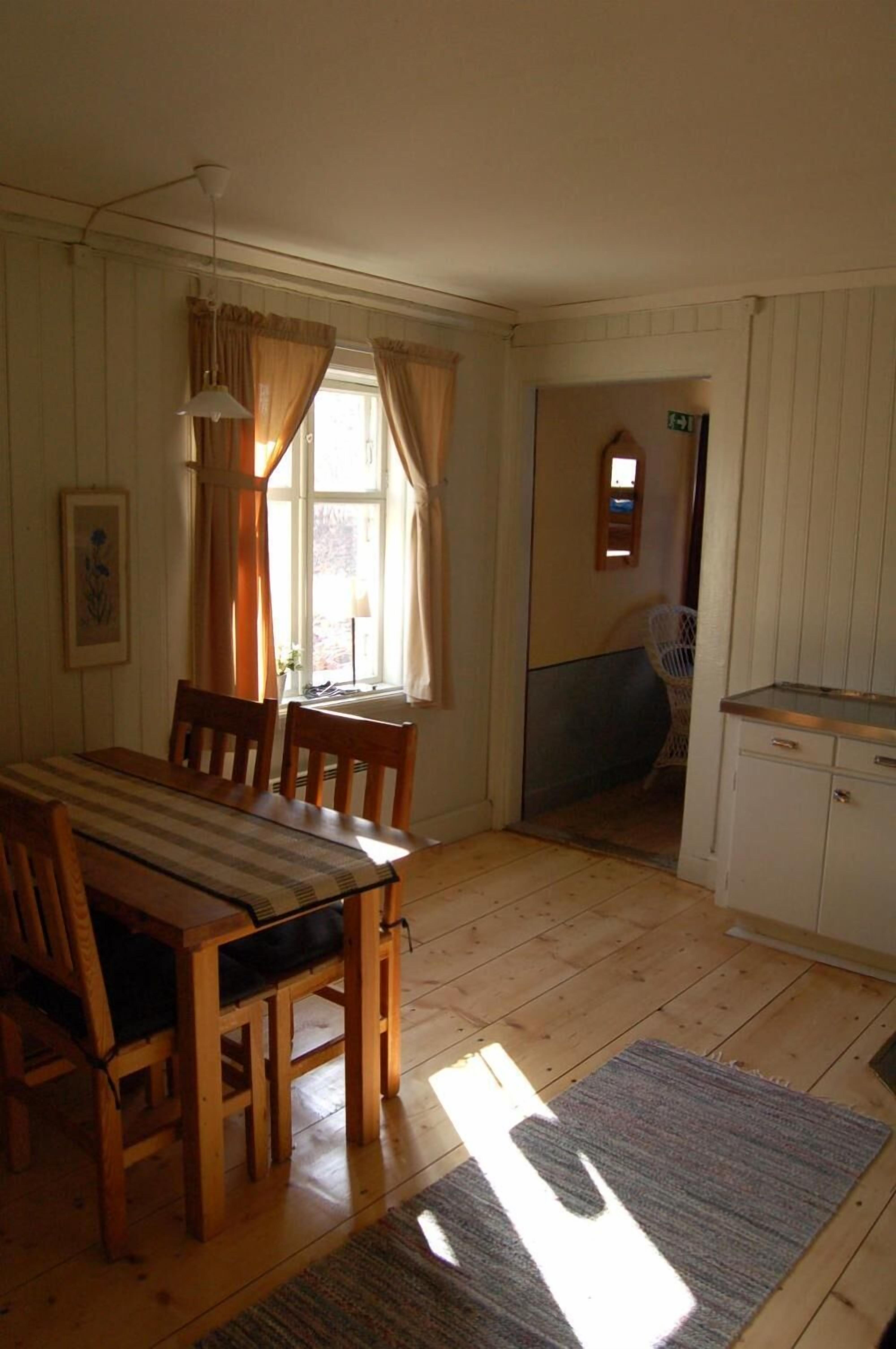 A dining area with a wooden table and chairs, a window with curtains, a small chair, and a cabinet.