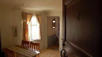 Una habitación con una mesa de madera y sillas, una ventana con cortinas y una puerta con manija.