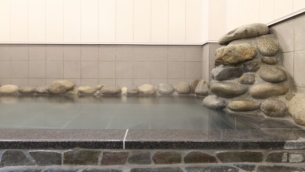 A stone-lined hot spring bath with a tiled wall and a stone ledge. - Kusatsu Onsen 326 Yamanoyu Hotel (Kusatsu)
